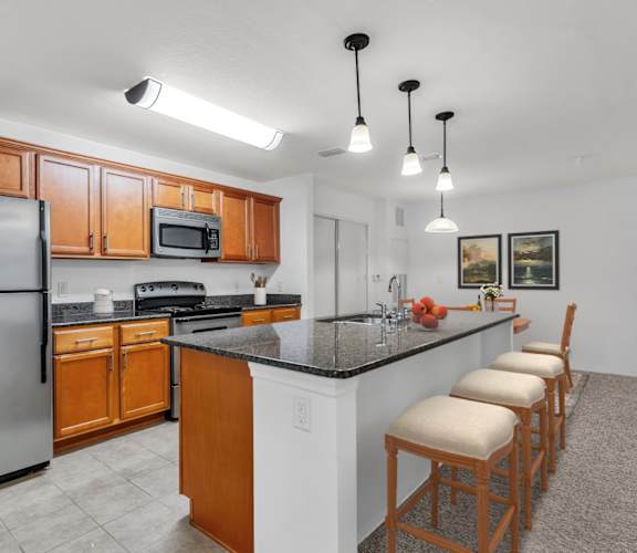 A kitchen with a refrigerator, microwave, and bar stools.