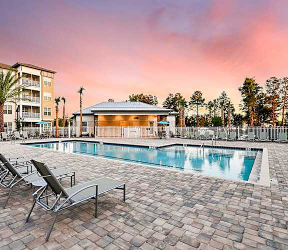A pool surrounded by chairs and a building in the background.
