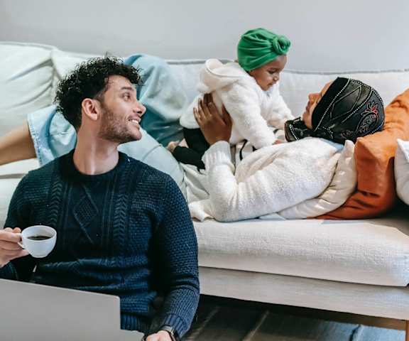 a man sitting on a couch with a cup of coffee and a laptop