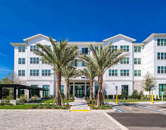 A large white building with a glass entrance and two palm trees in front. at Altis Twin Lakes Apartments, Kissimmee, FL 34744