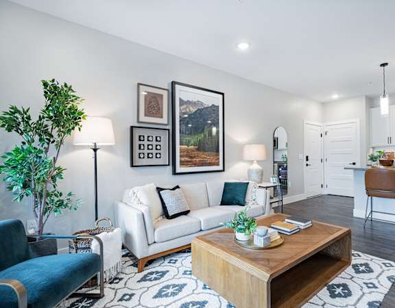 A modern living room with a white sofa, a wooden coffee table, and a kitchen area in the background.