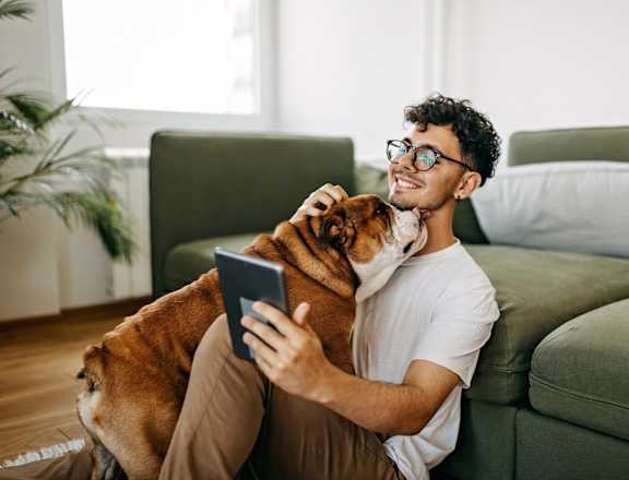 A man is sitting on a green couch with a dog and using a tablet.