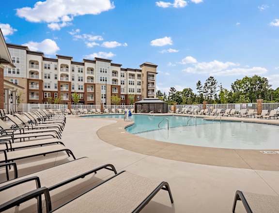 A large swimming pool surrounded by lounge chairs in front of apartment buildings at Ellis Station, NC, 27703