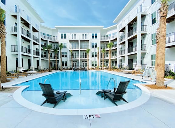 A swimming pool surrounded by palm trees and lounge chairs in front of apartment buildings.