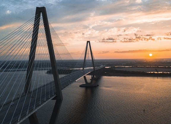 A bridge spans across a body of water with a sunset in the background.