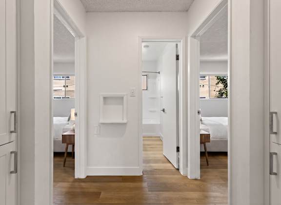 A white hallway with a bedroom and a bathroom visible through the door.