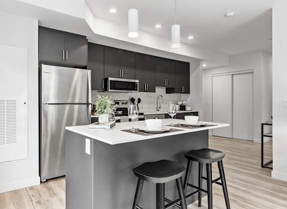 A modern kitchen with a white island and black bar stools.