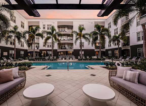 A pool surrounded by palm trees and lounge chairs.
