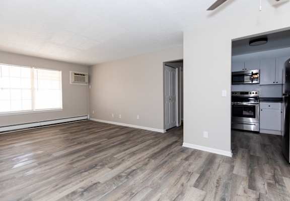 an empty living room with wood floors and a kitchen with stainless steel appliances