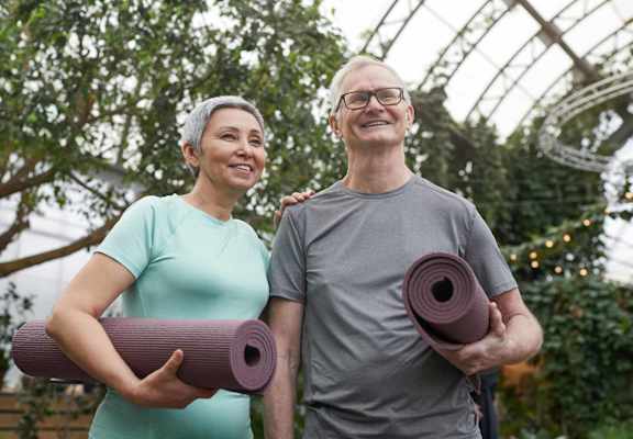 a man and a woman holding yoga mats in a greenhouse