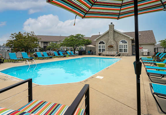 A pool with a striped umbrella and chairs.