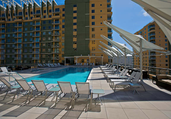 A pool surrounded by chairs and umbrellas with buildings in the background.