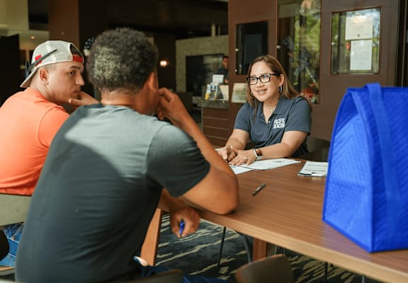 Three people sitting at a table with a blue bag in front of them.