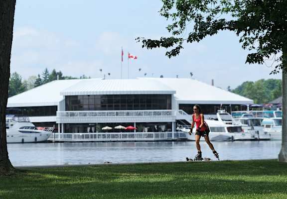 A woman is rollerblading in front of a white building with boats in the background.
