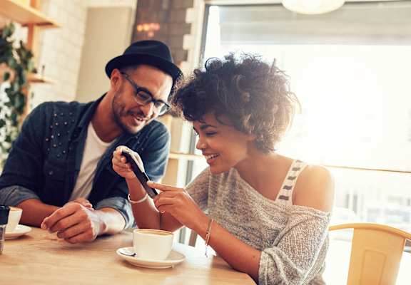 a man and woman sitting at a table looking at a cell phone