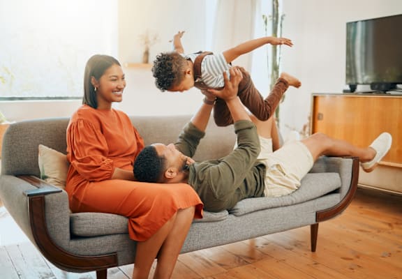 A family of three is having fun on a grey couch.