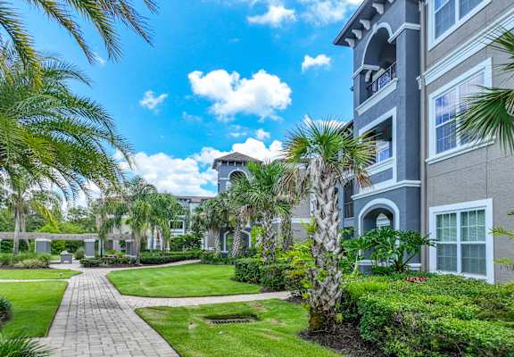 exterior building view with walking path and lush landscaping at The Reserves at Alafaya apartments