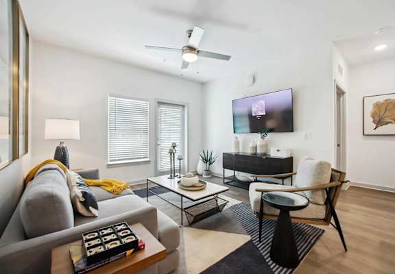 A modern living room with a grey sofa, a black coffee table, and a flat screen TV mounted on the wall.