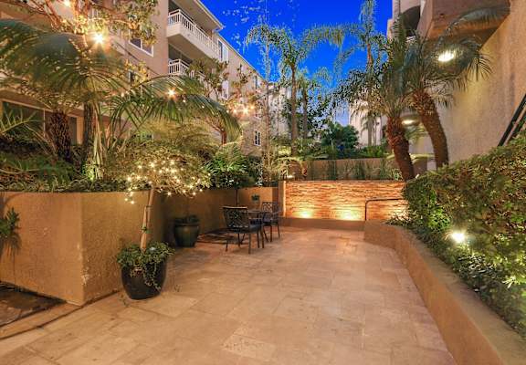 A patio with a table and chairs surrounded by plants and trees at Palm Royale Apartments, California