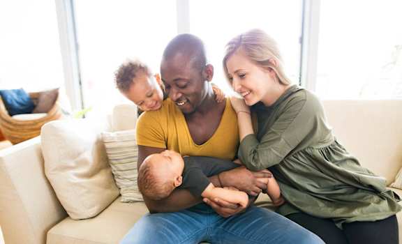 a family of three sitting on a couch with a baby Pineview Apartments in Clearwater, FL 33755