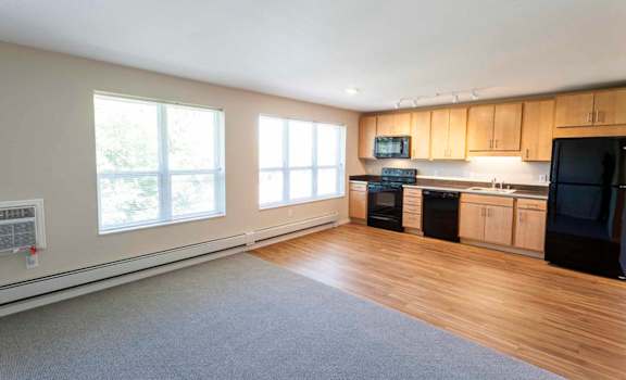 an empty living room with a kitchen in the background