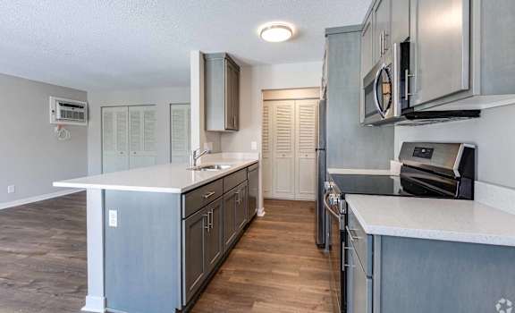 A kitchen with a white counter top and wooden floors.