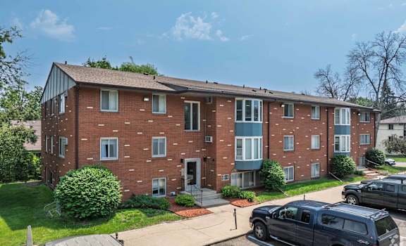 A red brick apartment building with a green bush in front.
