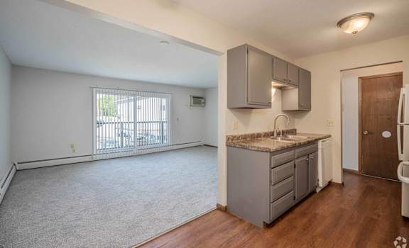A kitchen area with a sink, cabinets, and a window with blinds.