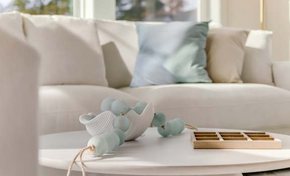 A white couch with a blue pillow and a white table with a wooden tray and blue decorations on it.