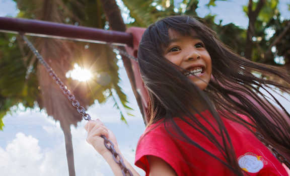 A girl in a red shirt is swinging on a swing set.