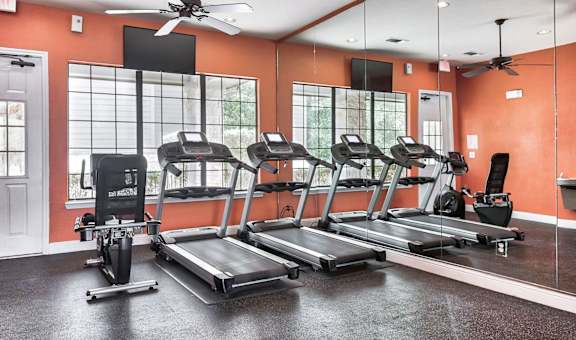 a fitness center with cardio equipment and large windows