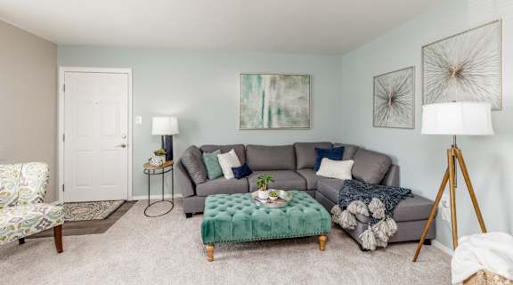 A living room with a grey couch, a green ottoman, and a painting on the wall.