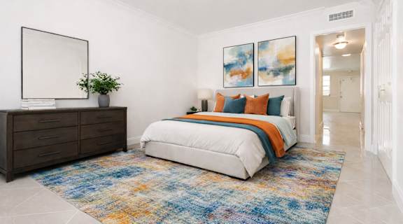 A bedroom with a white bed and a blue rug.