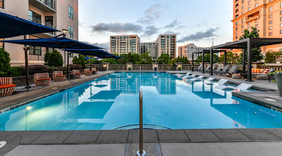a swimming pool with lounge chairs and umbrellas with a city skyline in the background