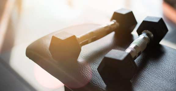 A pair of black dumbbells resting on a black mat.