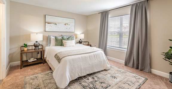 A bedroom with a large bed and a window with curtains.