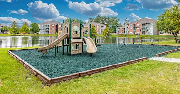 A playground with a green slide and a brown swing set.