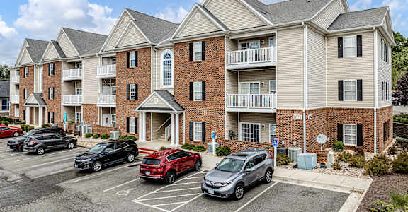 A red car is parked in a parking lot in front of a building.