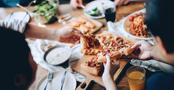 a group of people eating pizza at a table at Aura Stonebridge, Richmond