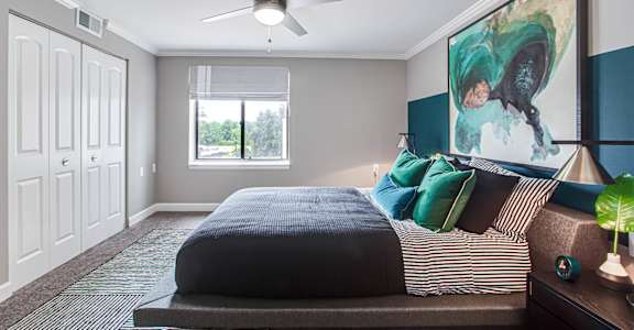 A bedroom with a bed, a ceiling fan, and a painting on the wall.