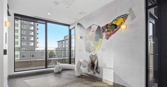 A white sculpture of a person with a colorful patterned head is on a wall in a room with a view of a building outside.
