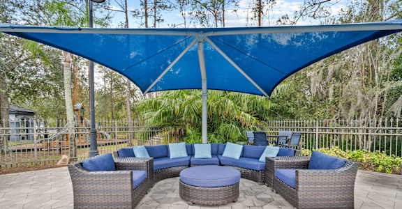 A patio with a blue canopy and grey wicker furniture at The Grand Reserve at Tampa Palms Apartments, Tampa, FL