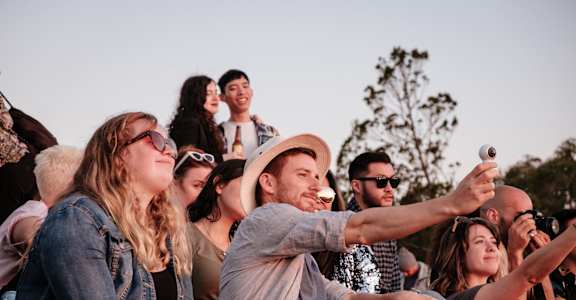 A group of people are sitting in a crowd, with one person taking a photo with a smartphone.