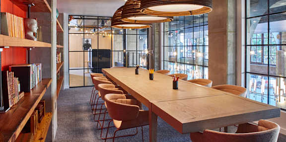 A long wooden table is surrounded by chairs in a room with a large window at The Platform in Norwalk, CT