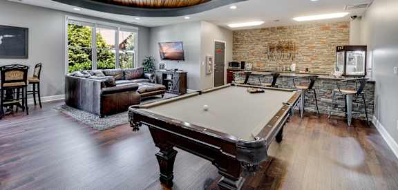A pool table is in the middle of a room with a brick wall.