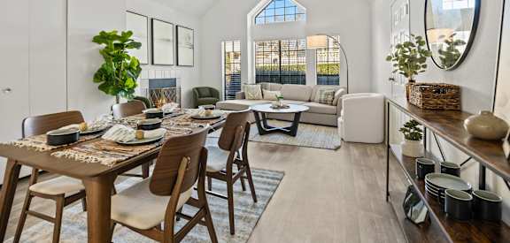 A dining room with a table set for six and a couch in the background.