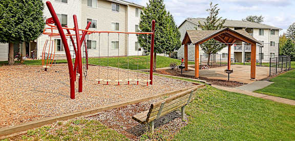 A playground with a red swing set and a wooden bench.
