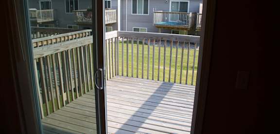 a sliding glass door opens to a deck with a house in the background