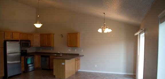 an empty living room with a kitchen in the background
