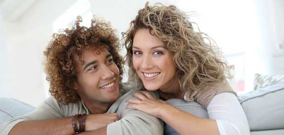 A man and a woman are sitting on a couch, smiling at each other.